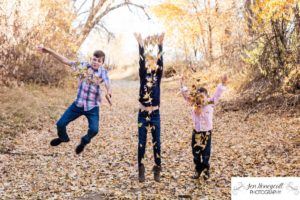 Littleton family photographer playing in leaves yellow trees fall in Colorado Highline Canal trail photography foothills outdoors nature throwing kids children