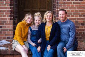 Littlleton family photographer Highlands Ranch Mansion stone building winter snow fall leaves red barn old building metal gate sisters big little girls teen teenagers foothills view at sunset